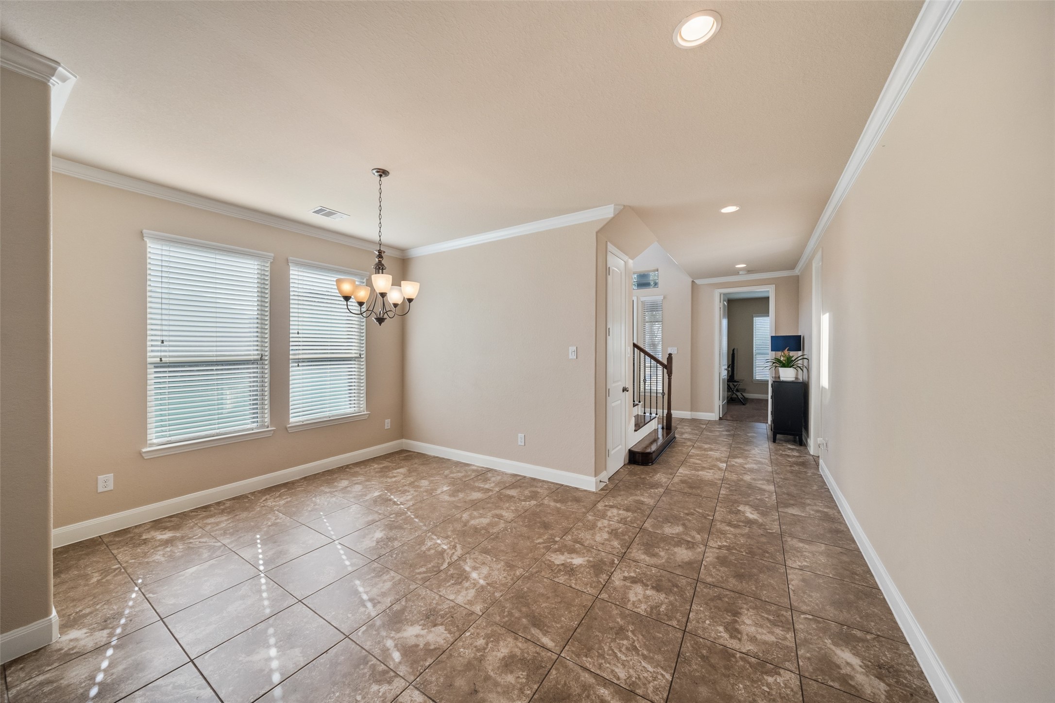 4747 Abercorn Street Rosharon, TX 77583 - Photo 10 of 46 Bright dining area with large windows and tile flooring, featuring a stylish chandelier. Adjacent hallway leads to other rooms, with a staircase for easy access to upper levels. Neutral tones create a welcoming ambiance.