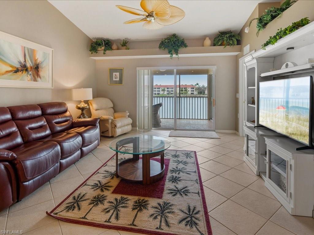 2810 Cypress Trace Circle, Unit 2127 Naples, FL 34119 - Photo 12 of 28 a living room with furniture a flat screen tv and a floor to ceiling window