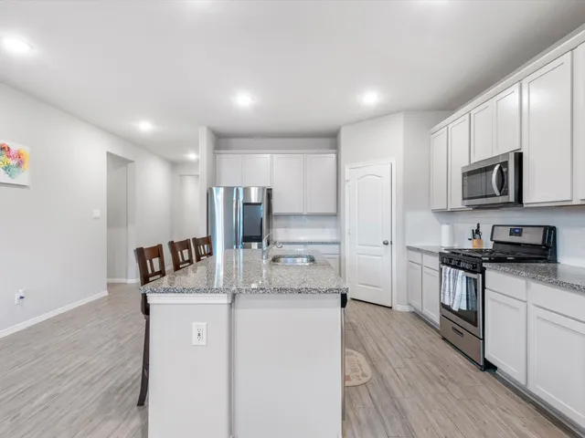 a kitchen with stainless steel appliances kitchen island granite countertop a stove a sink a refrigerator and white cabinets with wooden floor