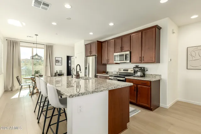 a kitchen with stainless steel appliances granite countertop a stove top oven a sink dishwasher a dining table and chairs with wooden floor