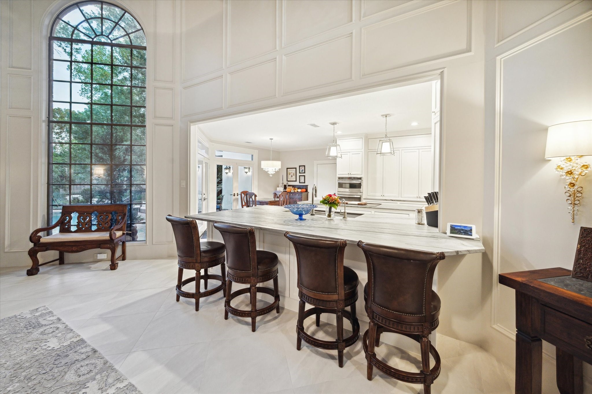 15406 Old Stone Trail Houston, TX 77079 - Photo 11 of 42 This is a spacious, elegant kitchen featuring a large center island with space for seating, white cabinetry, and a bright, airy atmosphere enhanced by a tall arched window providing ample natural light.