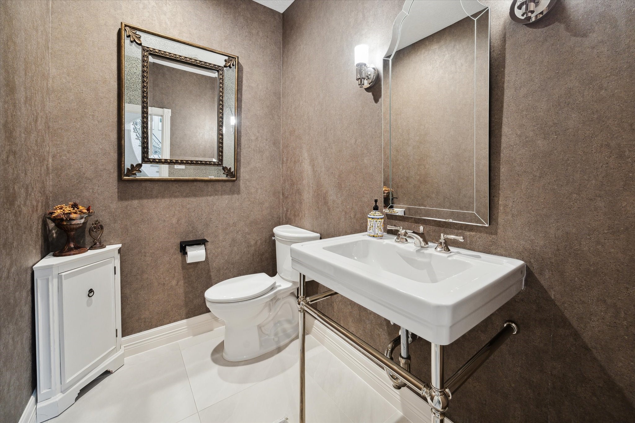 15406 Old Stone Trail Houston, TX 77079 - Photo 16 of 42 This is a modern half-bath with elegant finishes, featuring textured walls, a sleek pedestal sink, a classic framed mirror, complementary wall sconces, and a white tile floor.