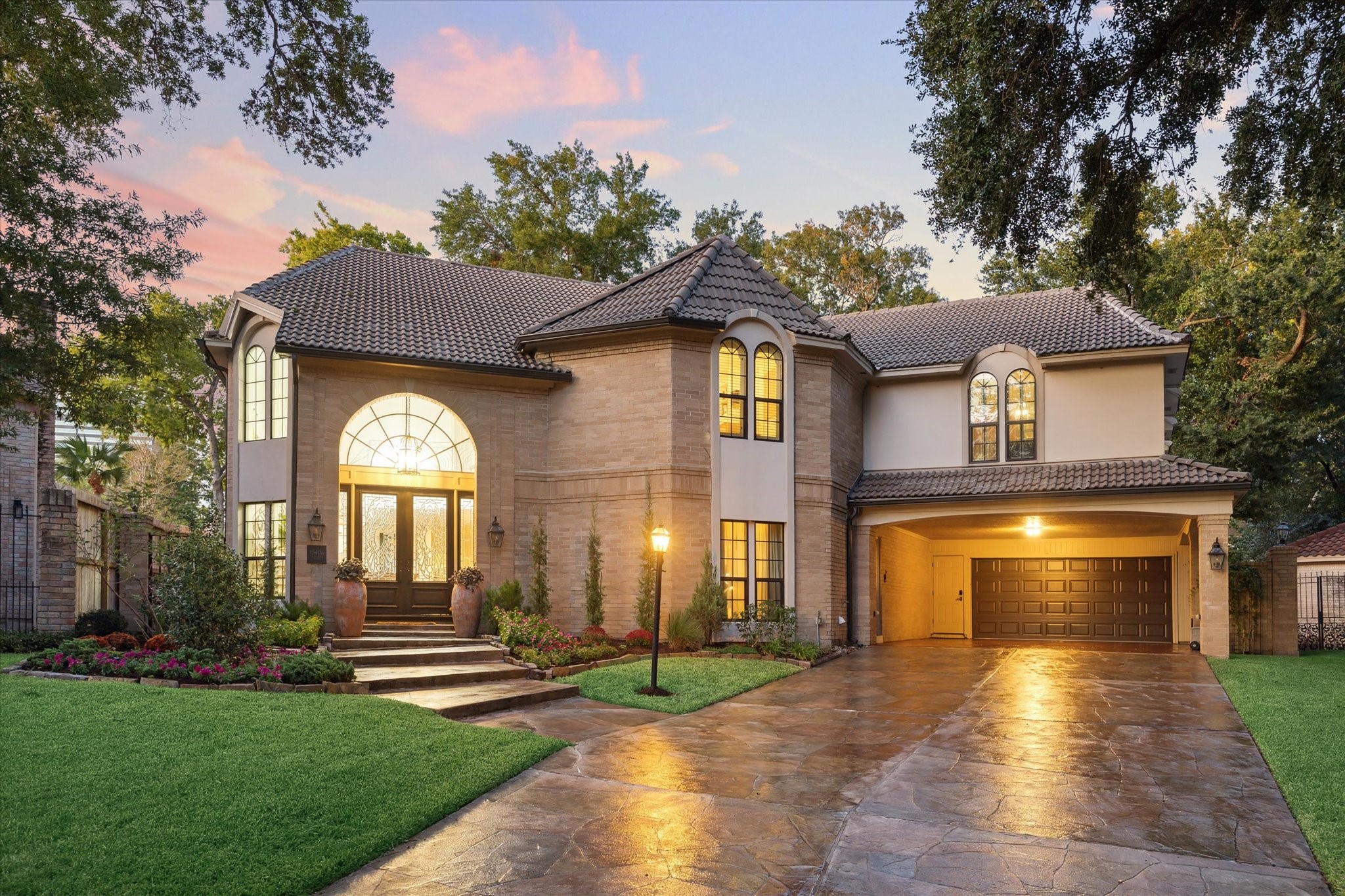 15406 Old Stone Trail Houston, TX 77079 - Photo 2 of 42 The exterior has a warm, neutral color palette, complemented by a tiled roof and elegant outdoor lighting, set in a peaceful neighborhood at dusk.
