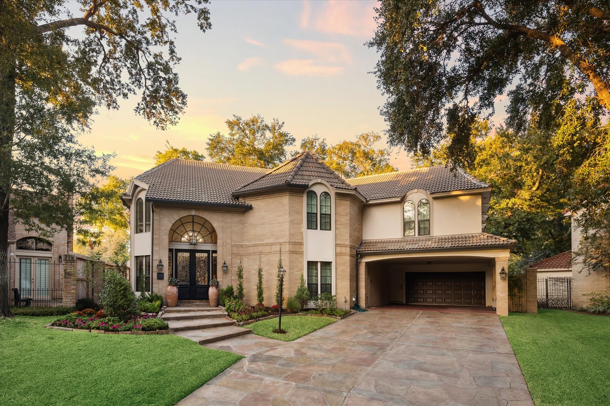 15406 Old Stone Trail Houston, TX 77079 - Photo 3 of 42 This elegant two-story home features a brick exterior, tile roof, and a spacious two-car garage. Landscaped with well-maintained greenery, it offers a welcoming entrance with a path leading to an arched front door, accented by outdoor lighting and flanked by large trees, giving the property a serene and established setting.