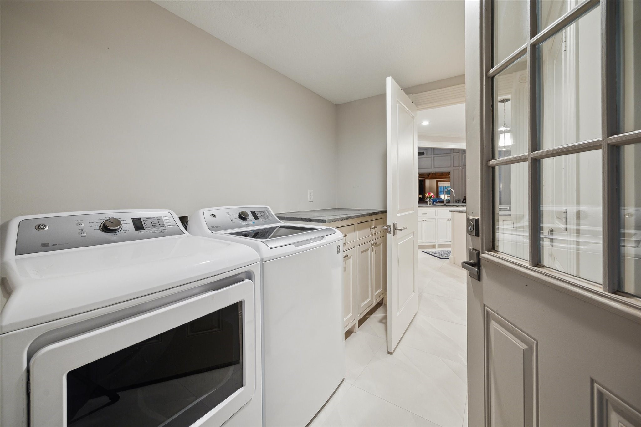 15406 Old Stone Trail Houston, TX 77079 - Photo 30 of 42 This is a modern laundry room featuring a washer and dryer set with a spacious countertop and ample cabinet storage. There's a large window providing natural light, and the room leads into a kitchen area.