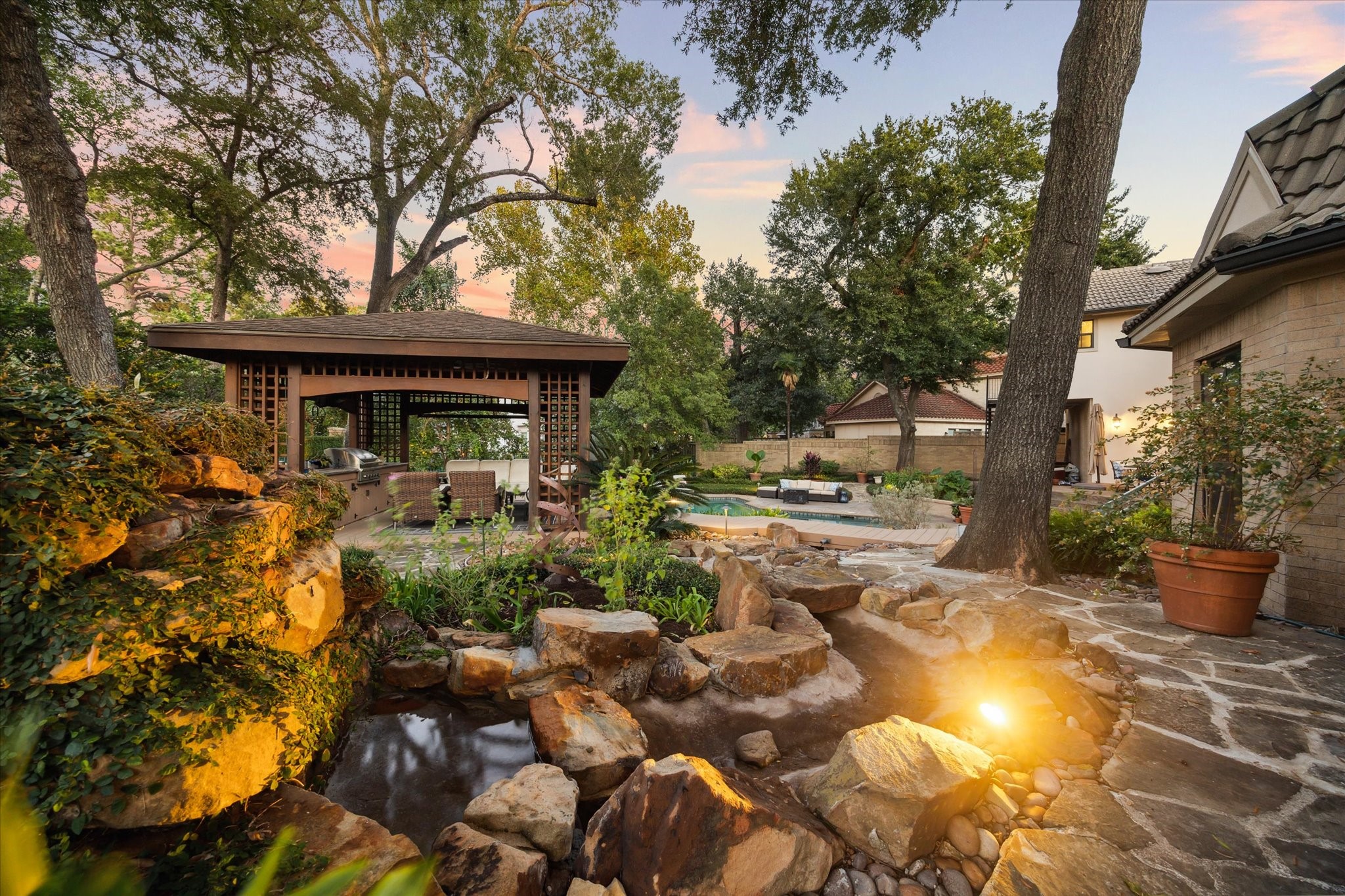 15406 Old Stone Trail Houston, TX 77079 - Photo 34 of 42 This property features a serene backyard oasis with a covered patio, lush landscaping, a picturesque rock stream, and a pool, perfect for relaxation and entertaining.