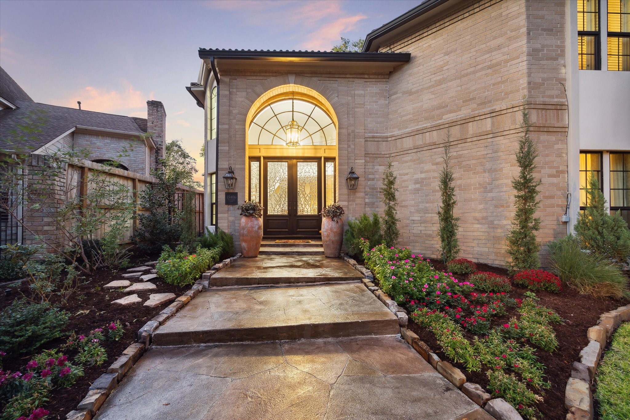 15406 Old Stone Trail Houston, TX 77079 - Photo 4 of 42 This is an elegant home entrance featuring a grand arched doorway with a decorative glass door, flanked by large windows. The pathway to the door is lined with well-manicured landscaping and stepping stones, creating a welcoming approach.