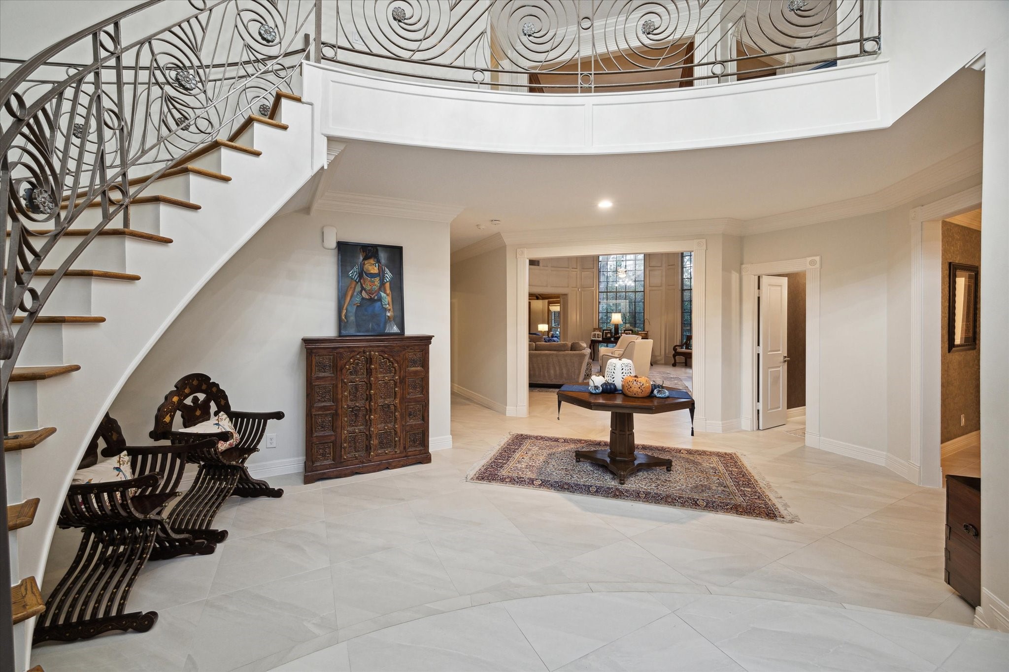 15406 Old Stone Trail Houston, TX 77079 - Photo 7 of 42 This is a spacious and elegant foyer with a sweeping staircase featuring intricate metal railings. The area is bright with natural light and has a high ceiling, creating an inviting entrance with an open feel. The view into adjacent rooms suggests a seamless flow throughout the home.
