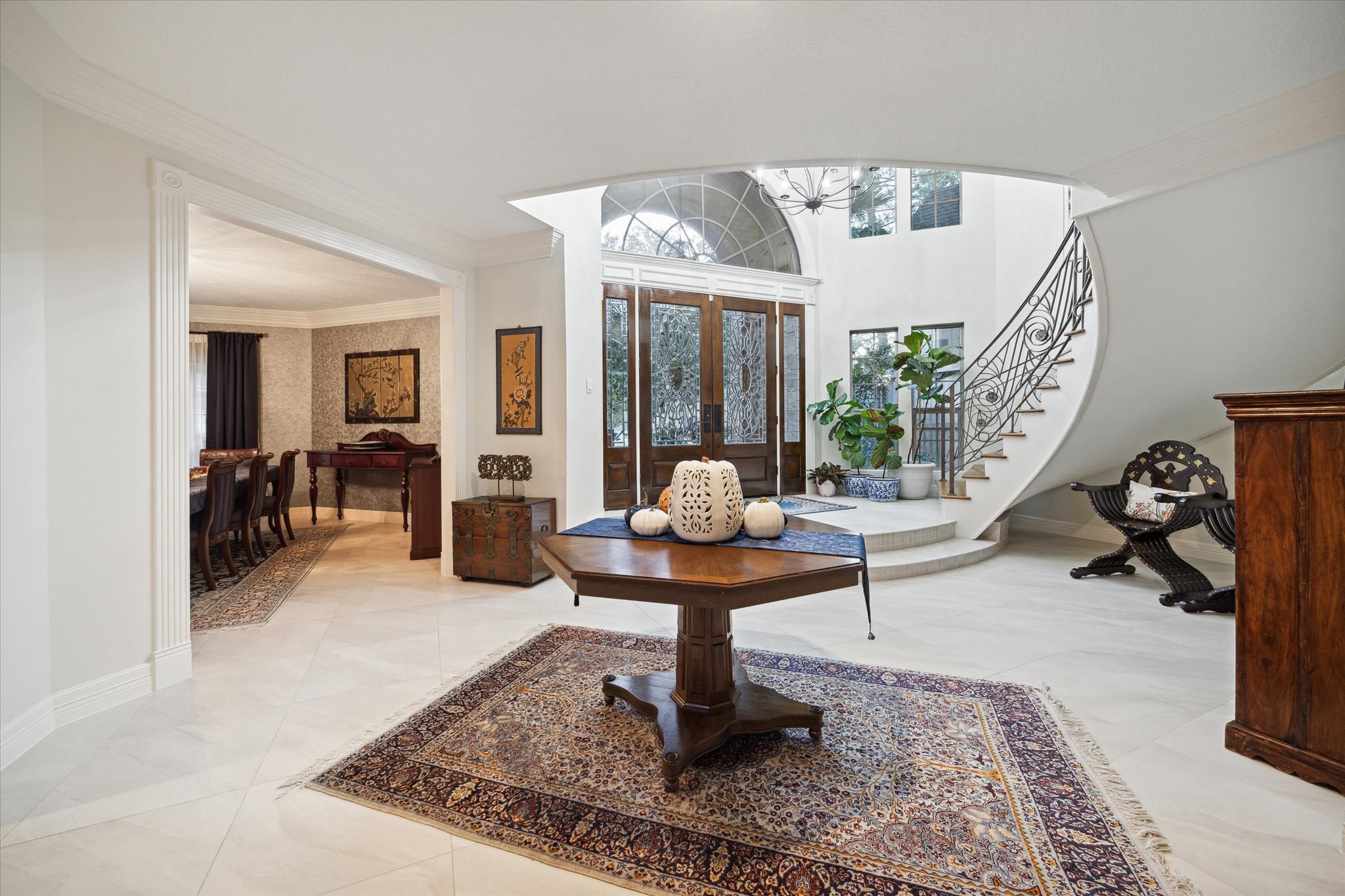 15406 Old Stone Trail Houston, TX 77079 - Photo 7 of 42 This is an elegant entryway with a sweeping staircase, high ceilings, and bright natural light, leading into a formal dining area.