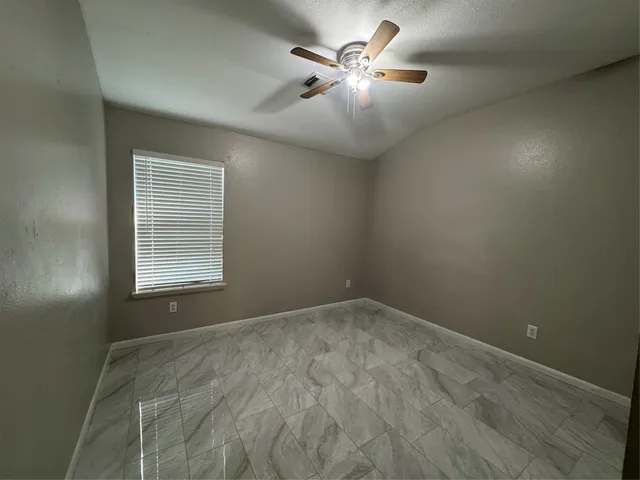 an empty room with a chandelier fan and windows