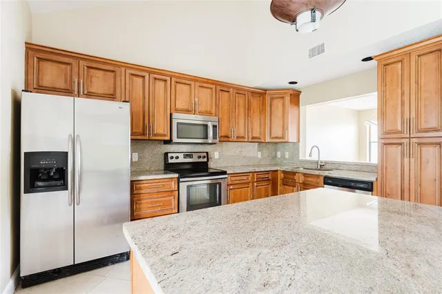 a kitchen with granite countertop wooden cabinets a refrigerator stove top oven and sink
