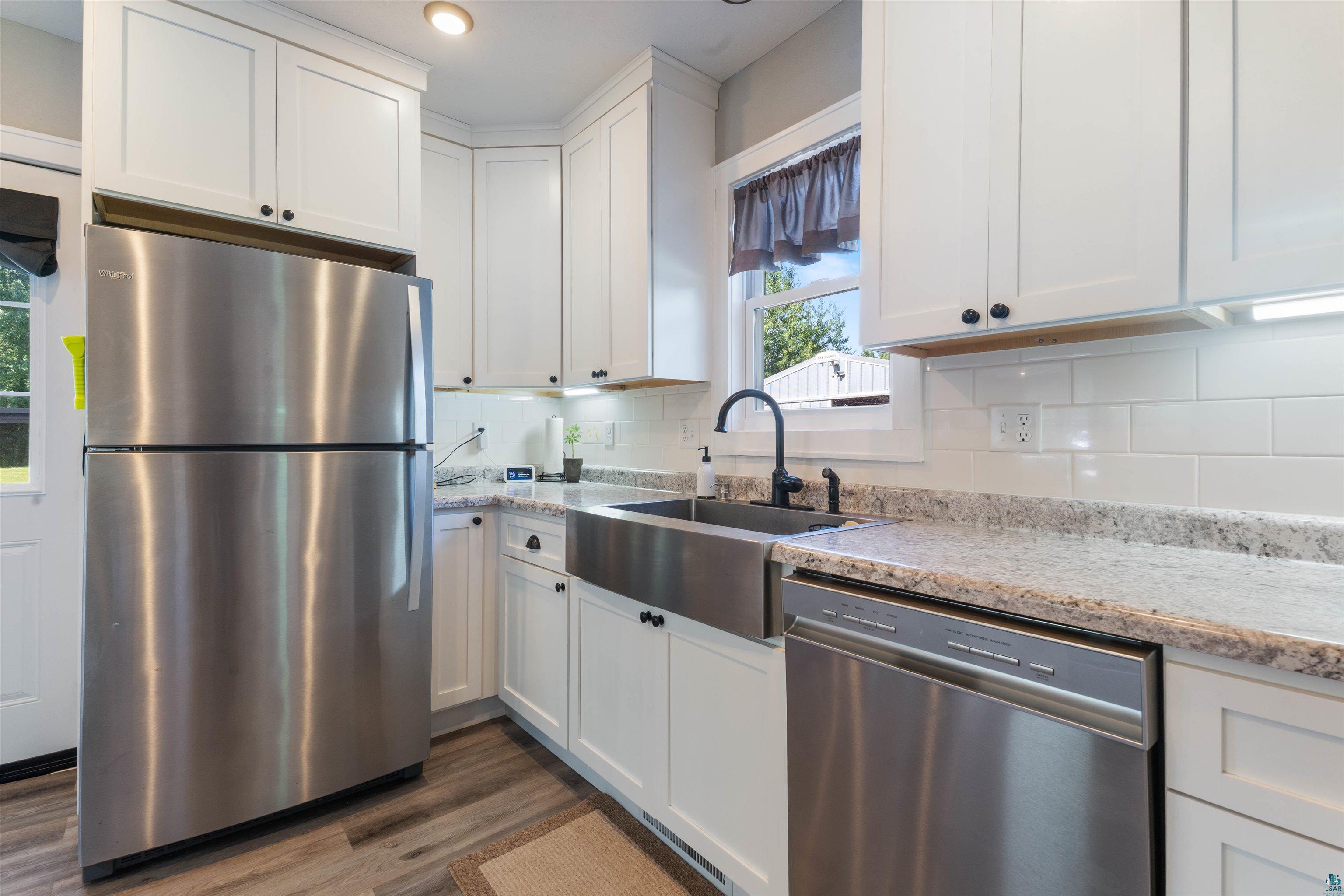 3835 South County Rd K South Range, WI 54874 - Photo 7 of 29 Modern kitchen featuring white shaker cabinetry, stainless steel appliances, speckled stone countertops, a farmhouse sink with a matte black faucet, and wood-finish flooring