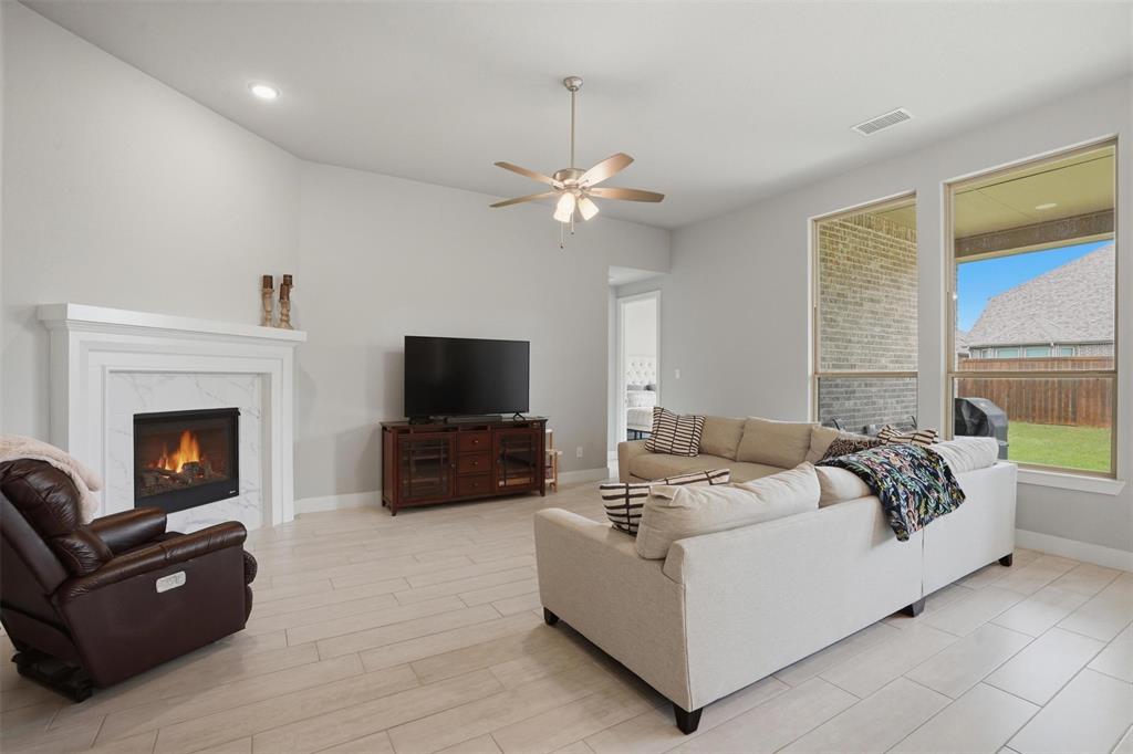 1429 Eclipse Road Aubrey, TX 76227 - Photo 6 of 37 Living area featuring light-colored tile flooring, a fireplace with a white mantel and marble surround, and a ceiling fan