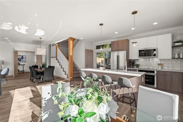 a kitchen with stainless steel appliances kitchen island granite countertop a refrigerator a stove a sink a dining table and chairs with wooden floor