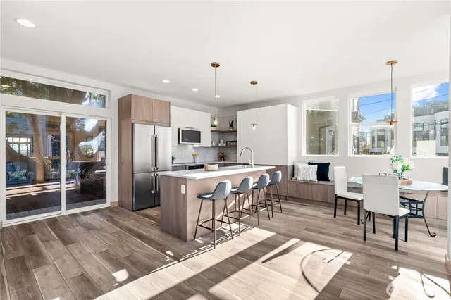 a living room with stainless steel appliances kitchen island granite countertop a refrigerator a stove top oven and a dining table with wooden floor