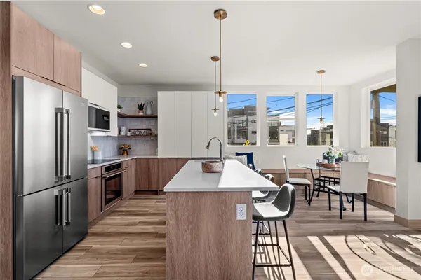 a kitchen with stainless steel appliances kitchen island granite countertop a refrigerator a stove and a dining table with wooden floor