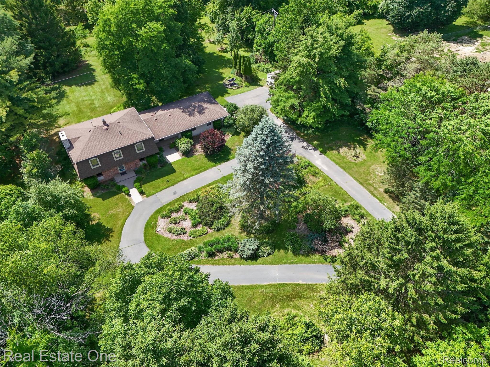 6039 Fish Lake Road Holly, MI 48442 - Photo 50 of 64 Sprawling property featuring a stone and brick façade, a brown shingle roof, extensive green landscaping, a paved circular driveway, and mature trees and gardens.