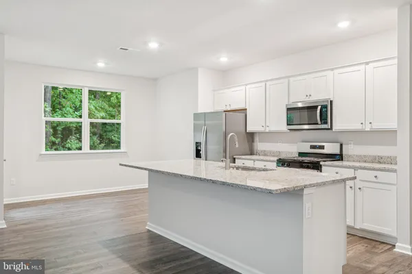 a kitchen with stainless steel appliances granite countertop a sink a stove a microwave a refrigerator a window and white cabinets