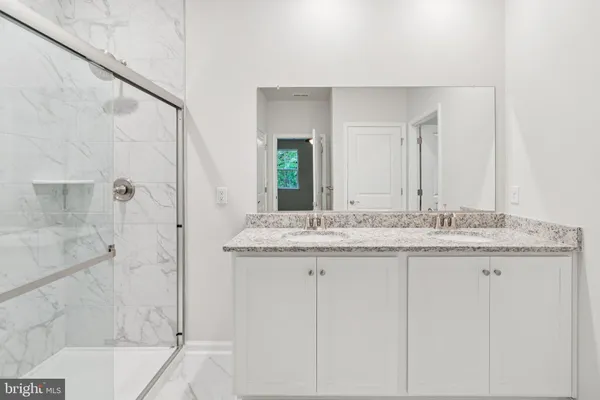 a bathroom with a granite countertop sink two mirror and shower