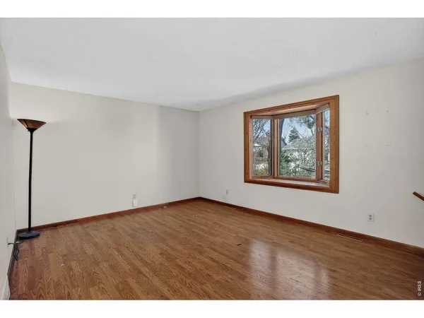 a view of an empty room with a window and wooden floor