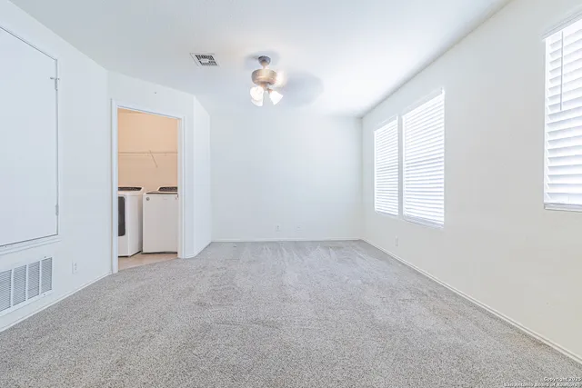 an empty room with chandelier fan and windows