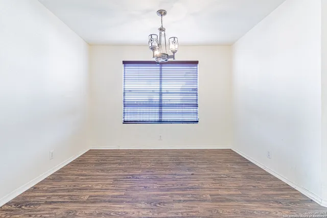 an empty room with wooden floor chandelier and windows