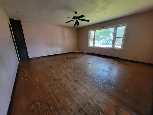 an empty room with wooden floor fan and windows