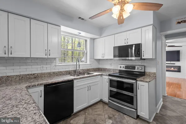 a kitchen with stainless steel appliances granite countertop a sink dishwasher a stove top oven a refrigerator with grey cabinets and wooden floor