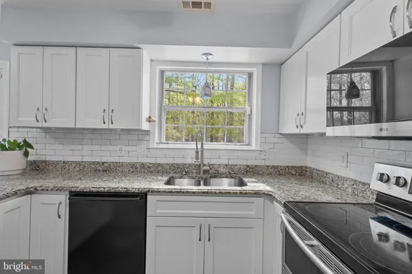 a kitchen with granite countertop a sink stainless steel appliances white cabinets and a window