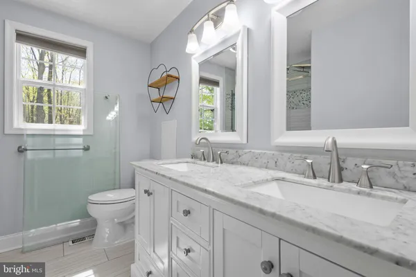 a bathroom with a granite countertop toilet a sink a mirror a window and a shower