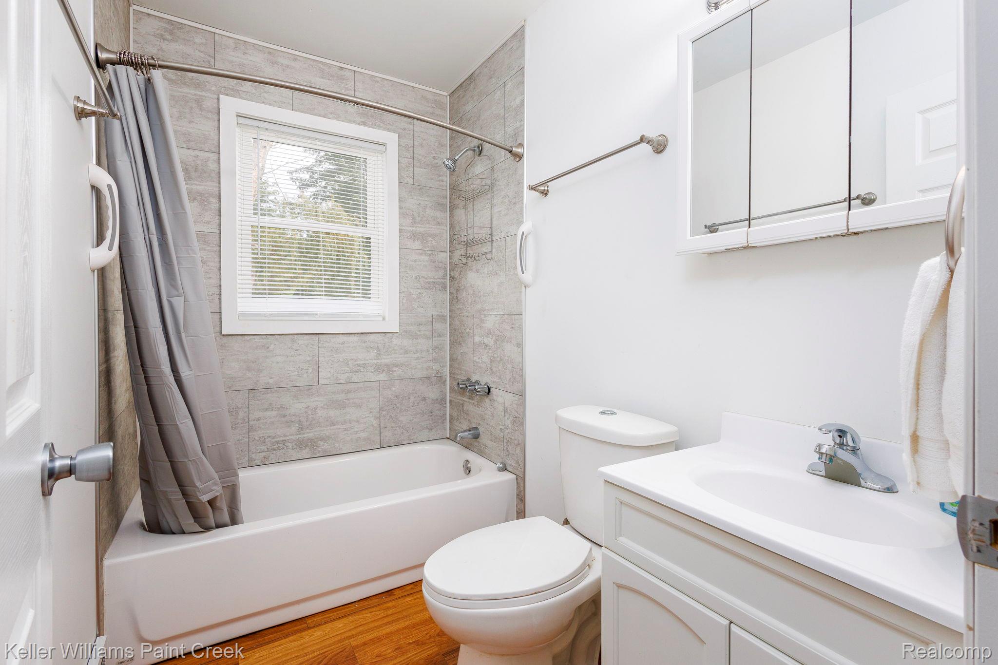 2244 Hammerslea Road Lake Orion, MI 48359 - Photo 13 of 21 Bathroom featuring wood-finish flooring, a built-in bathtub with tiled surround, a window with blinds, and a vanity with an integrated sink