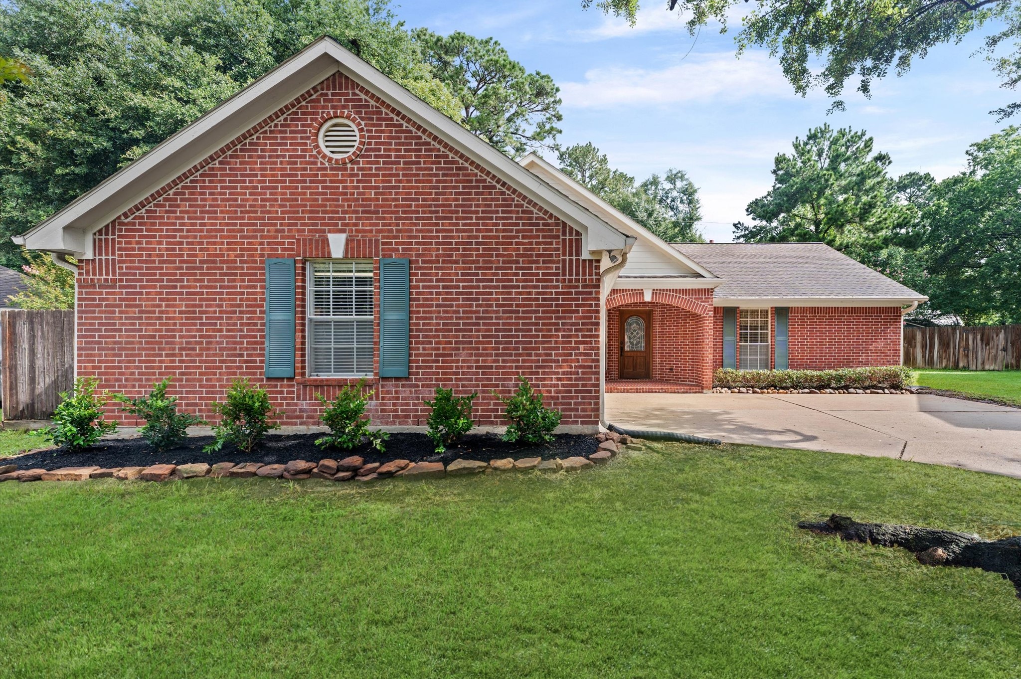 17618 Mill Springs Drive Spring, TX 77379 - Photo 2 of 26 This photo showcases a charming red brick home with a well-maintained lawn and landscaped garden. The house features a gabled roof, blue shutters, and a welcoming front porch. A spacious driveway leads to the main entrance, surrounded by mature trees.
