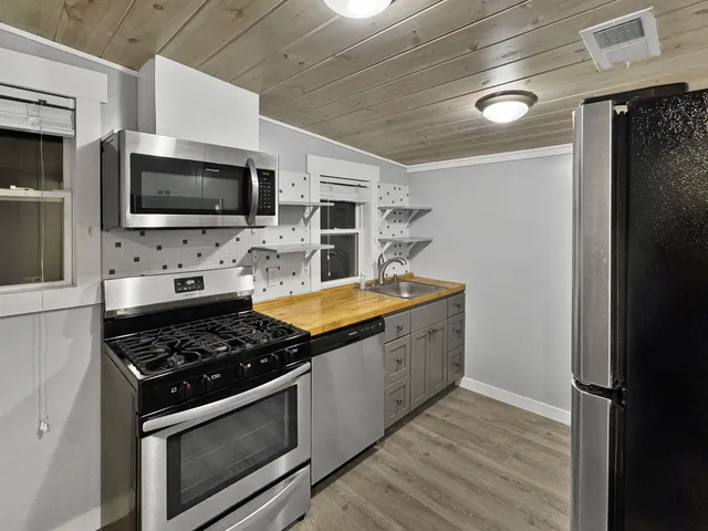 a kitchen with stainless steel appliances granite countertop a stove top oven a sink dishwasher a refrigerator and a microwave oven with white cabinets