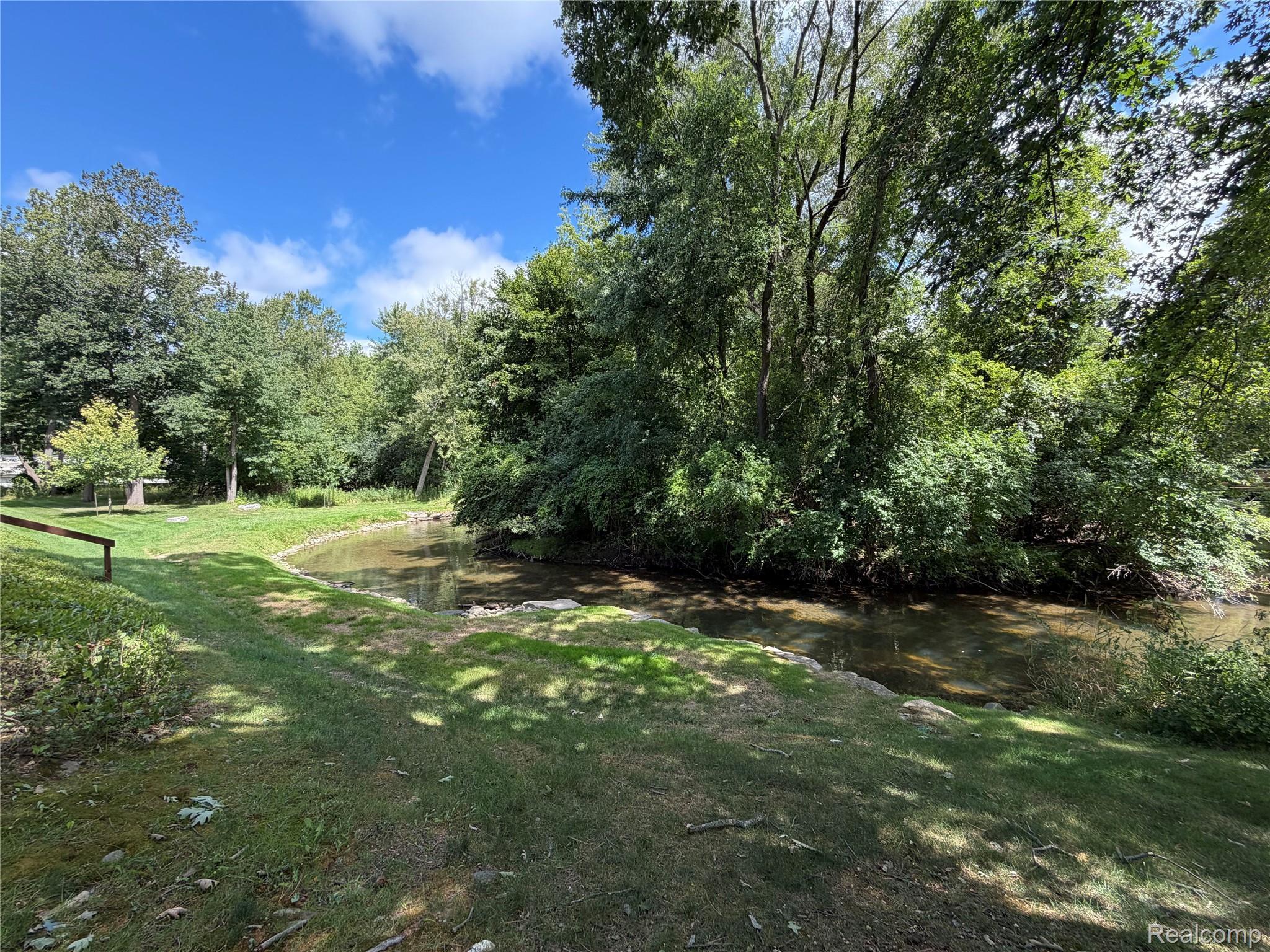 629 Oakbrook West, Unit 18 Rochester, MI 48307 - Photo 2 of 22 Expansive grassy area bordering a natural waterway, featuring mature trees and established greenery