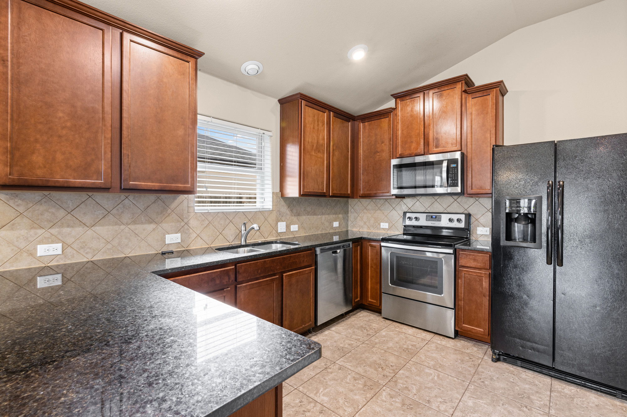 19308 Stokes Lane Pflugerville, TX 78660 - Photo 6 of 27 Kitchen featuring dark wood cabinetry, a diagonally tiled backsplash, dark countertops, and stainless steel appliances