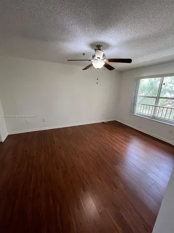 an empty room with wooden floor fan and windows