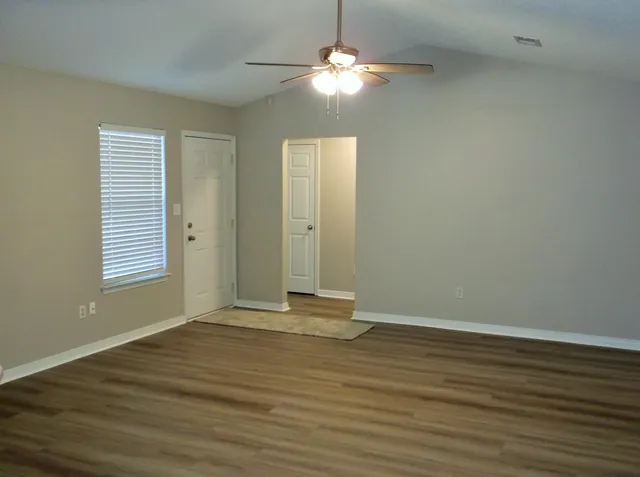 an empty room with wooden floor chandelier fan and windows