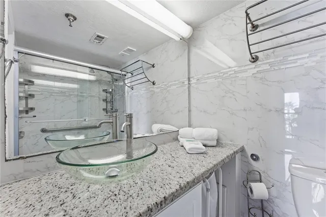 a bathroom with a granite countertop sink a toilet a mirror and shower