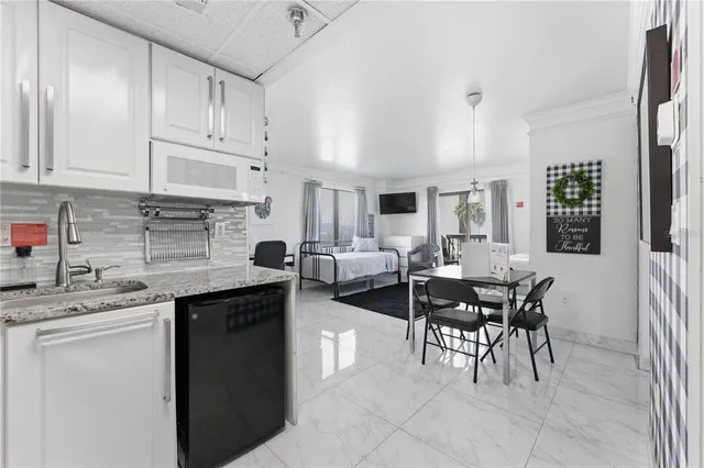 a open kitchen with stainless steel appliances granite countertop a stove top oven a sink a dining table and chairs with white cabinets