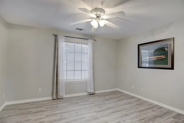 an empty room with wooden floor chandelier fan and windows