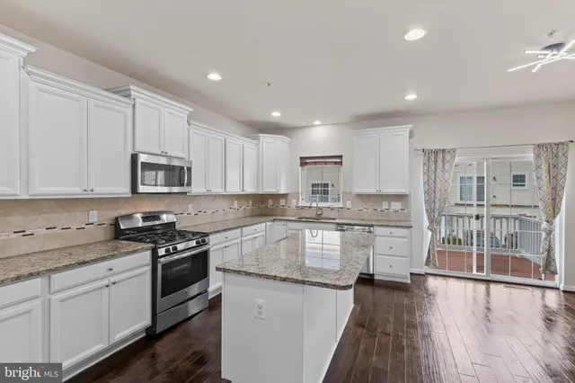 a kitchen with stainless steel appliances granite countertop a stove top oven a sink a refrigerator white cabinets and wooden floor