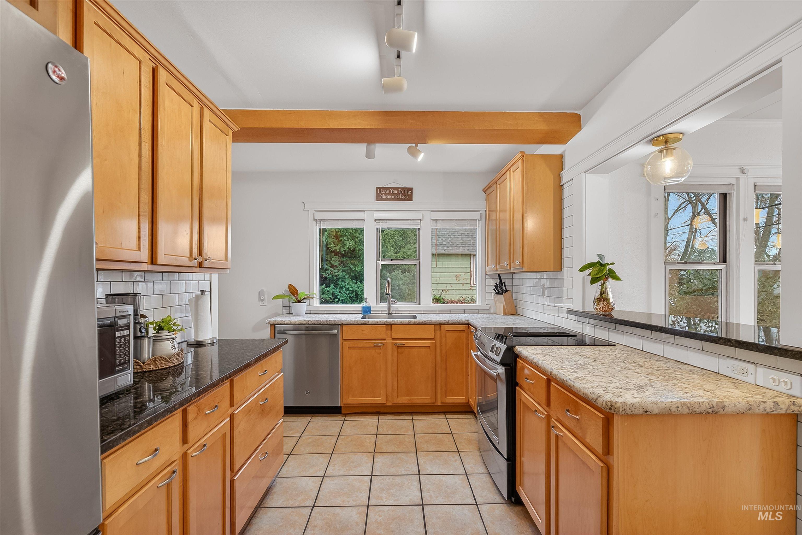 1209 3rd Street Lewiston, ID 83501 - Photo 10 of 49 Kitchen featuring appliances with stainless steel finishes, dark stone countertops, light tile patterned floors, beamed ceiling, and tasteful backsplash