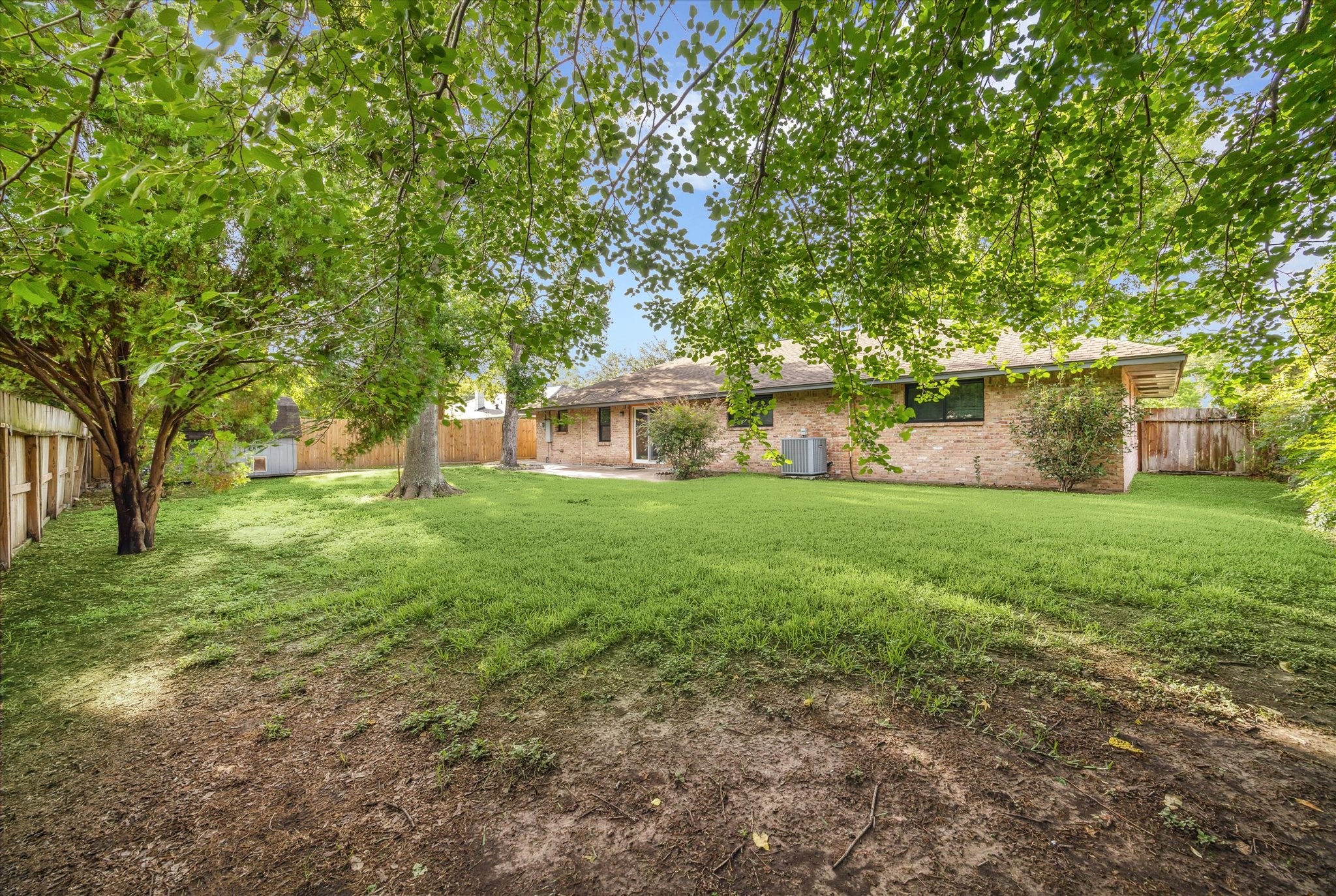8907 Autauga Street Houston, TX 77080 - Photo 20 of 20 This photo features a spacious backyard with lush green grass and mature trees, providing ample shade. The brick exterior of the house offers a classic look, and the yard is enclosed by a wooden fence, offering privacy and a serene outdoor space.
