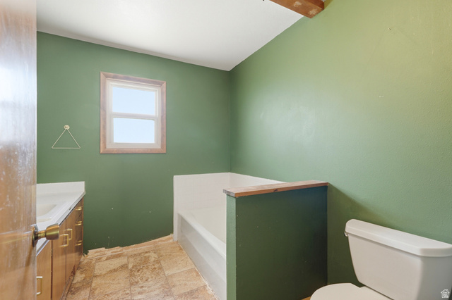 1410 Sumac Drive Logan, UT 84321 - Photo 12 of 28 Bathroom featuring a single vanity with wood-finish cabinetry, a window with wood trim, a built-in bathtub, and a toilet