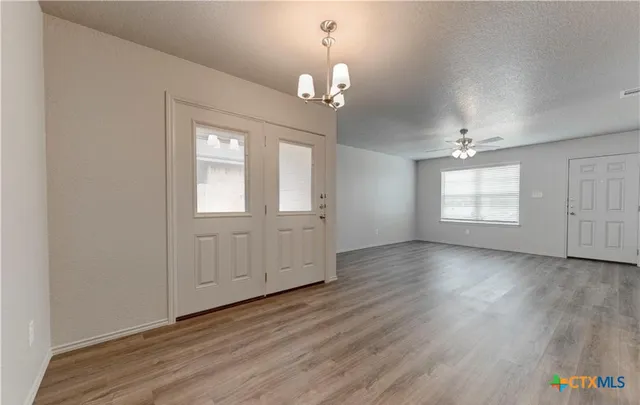 an empty room with wooden floor chandelier and windows