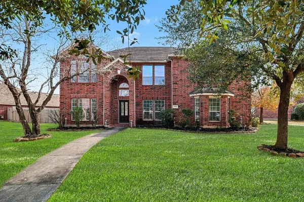 a view of a brick house with a big yard and large trees