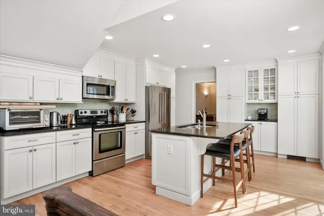 a kitchen with stainless steel appliances granite countertop a stove top oven a sink dishwasher a refrigerator and white cabinets with wooden floor
