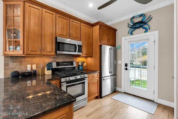 a kitchen with stainless steel appliances granite countertop wooden cabinets a sink dishwasher a stove and a refrigerator with wooden floor