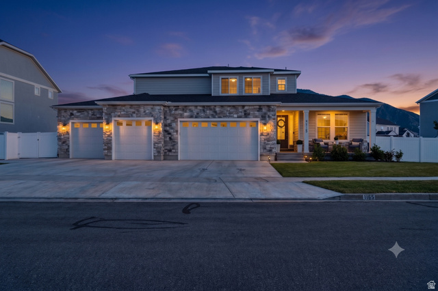 Contemporary residence featuring a three-car garage, stone and siding exterior, a covered porch, and a manicured front lawn