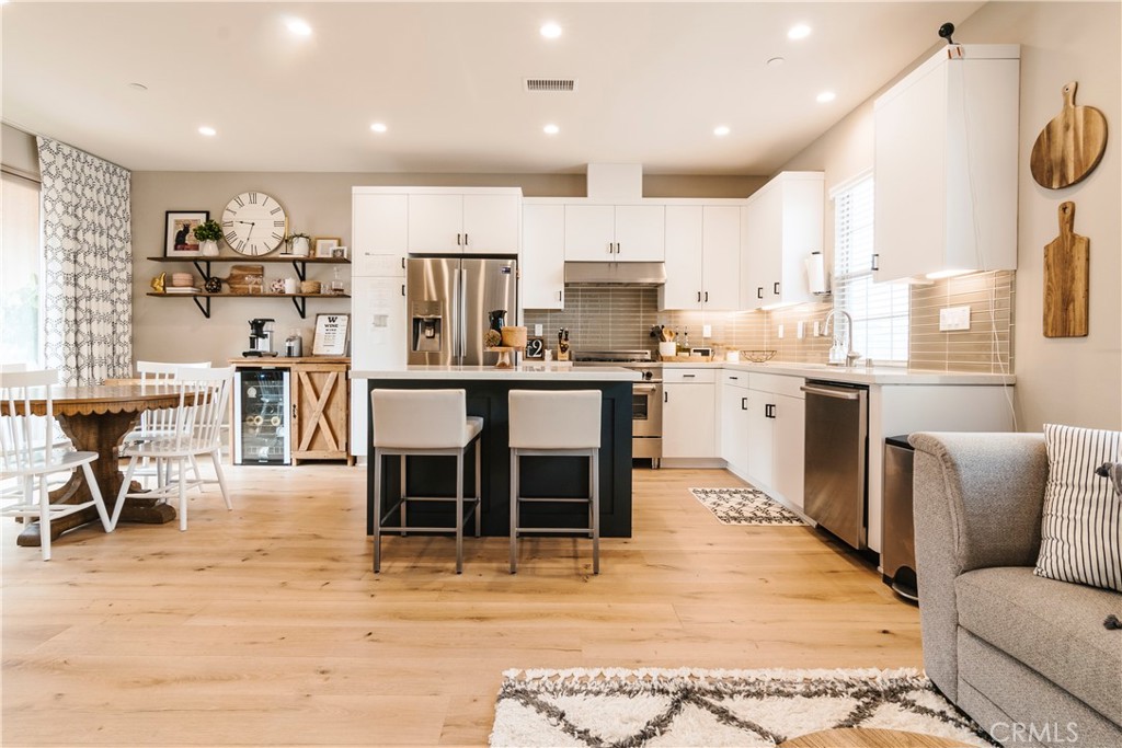 a living room with stainless steel appliances kitchen island granite countertop a dining table chairs sink and cabinets